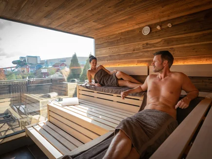 Pärchen sitzt in einer Panoramasauna im Hotel  "Krønasår" mit Blick auf die Wasserwelt Rulantica.