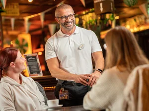 Eine Servicekraft in einem der Restaurants im Europa-Park Erlebnis-Resort bei der Arbeit. Er ist im Gespräch mit zwei Gästen.
