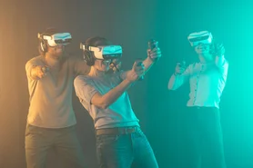 Drei Personen mit VR-Brillen, Headsets und Controllern bei YULLBE GO in einem bunt beleuchtetem Raum.