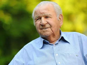 Franz Mack lächelnd im karierten Hemd in sonniger, grüner Umgebung mit unscharfem Hintergrund