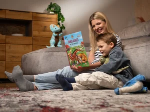 Mutter sitzt neben ihrem kleinen Sohn und liest ihm aus dem Madame Freudenreich Kinderbuch vor.