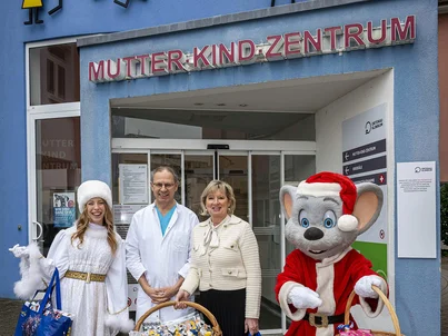 Mauritia Mack, Ed Euromaus und ein Weihnachtsengel verteilen Geschenke in einem Mutter-Kind-Zentrum.