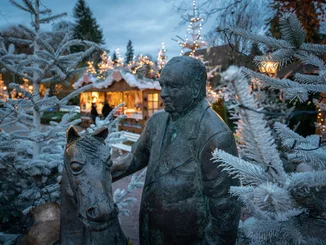 Bronzestatue von Franz Mack mit einem Pferd zwischen geschmückten Weihnachtsbäumen auf dem Europa-Park Weihnachtsmarkt.