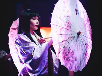 Eine Tänzerin der Europa-Park Dinner-Show mit auffälligem Kostüm und einem Sonnenschirm.