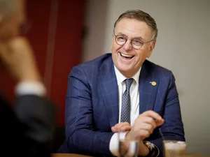 Roland Mack sitzt an einem Besprechungstisch und lächelt.