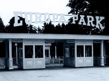 Former main entrance to Europa-Park with four ticket booths and lettering, surrounded by tall trees.