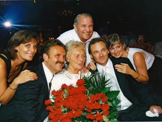 Familienfoto der Familie Mack beim 75. Geburtstag von Liesel Mack, die in der Mitte steht und einen großen Strauß roter Rosen hält.