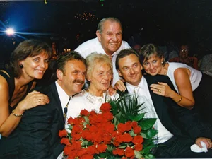 Familienfoto der Familie Mack beim 75. Geburtstag von Liesel Mack, die in der Mitte steht und einen großen Strauß roter Rosen hält.