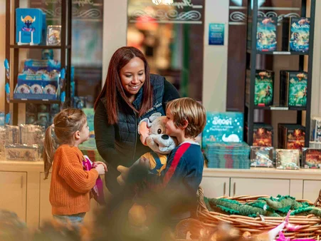 Une collaboratrice d’une boutique de souvenirs à Europa-Park présente une peluche Ed Euromaus à deux enfants, ravis.