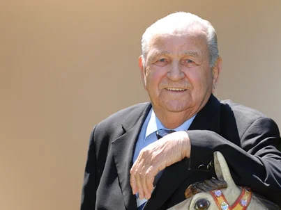 Portrait von Europa-Park Gründer Franz Mack, der sich auf ein Karussellpferd lehnt.