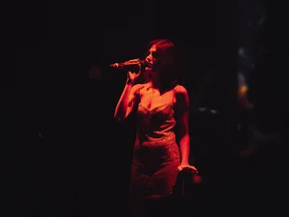 Eine Frau singt im Dunklen, sie wird nur von einer Lampe beleuchtet.