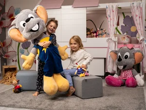 Zwei Kinder in ihrem Kinderzimmer haben große Plüsch-Euromäuse, mit denen sie spielen.