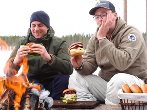 Thomas Mack und Brian Bojsen essen Burger am Lagerfeuer.