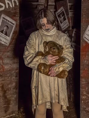 Eine junge Darstellerin trägt einen Teddybär im Arm in der Scare Attraction The Hill bei Traumatica.